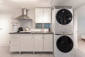 A modern kitchen with a built-in washer and dryer, a coffee machine, and a window above the sink. - Seoul Pause (Mapo-gu)