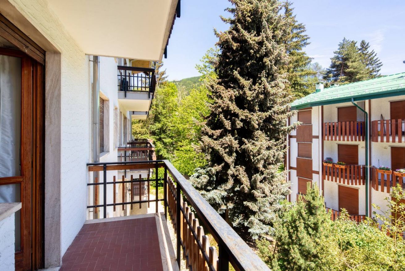 Ein Gebäude mit einem Balkon, einem großen immergrünen Baum und Blick auf einen Berg.