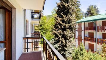 Ein Gebäude mit einem Balkon, einem großen immergrünen Baum und Blick auf einen Berg.
