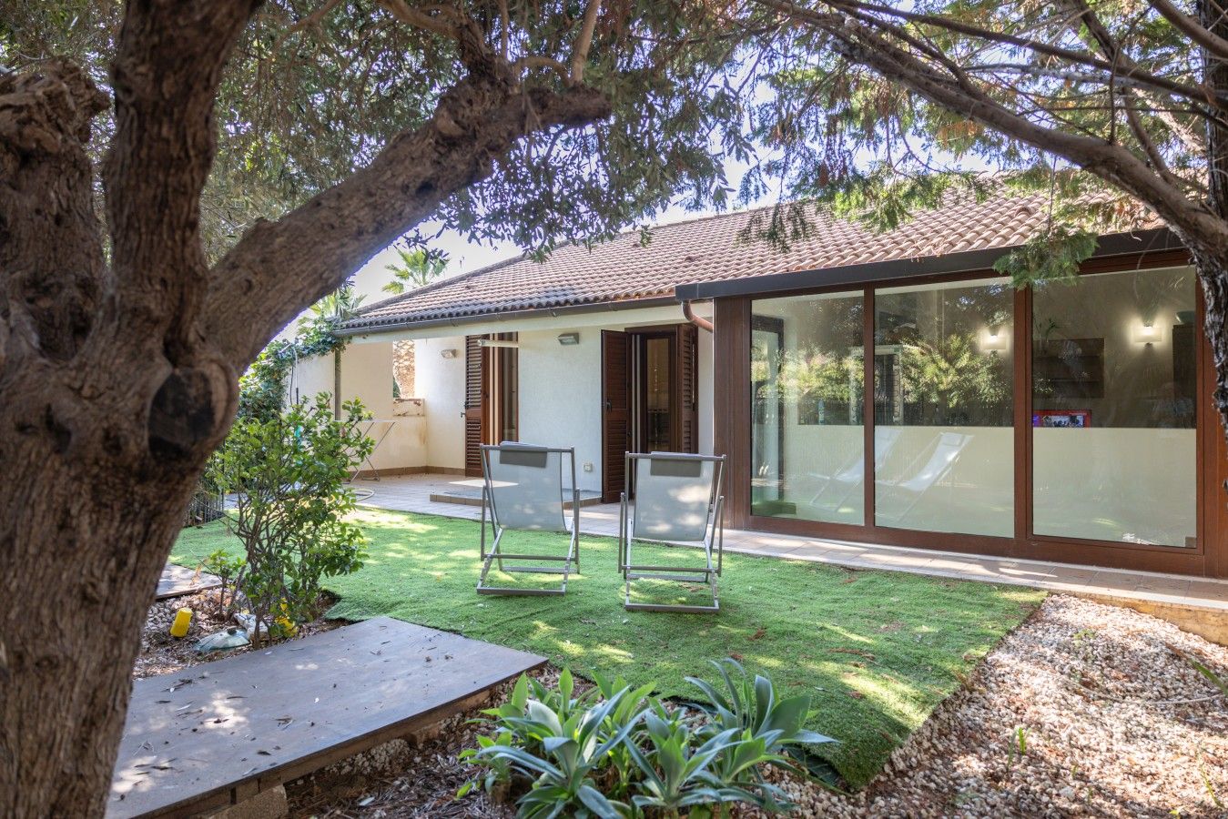 Une maison moderne dotée d’un patio, d’un grand arbre et offrant une vue dégagée sur les environs.