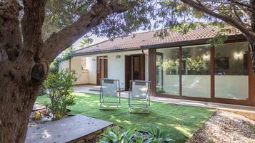 Une maison moderne dotée d’un patio, d’un grand arbre et offrant une vue dégagée sur les environs.