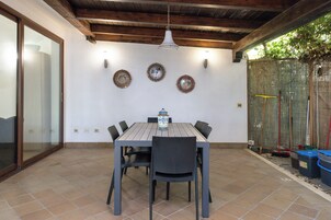 Um pátio externo com mesa e cadeiras de madeira, cercado por um muro branco com pratos decorativos.