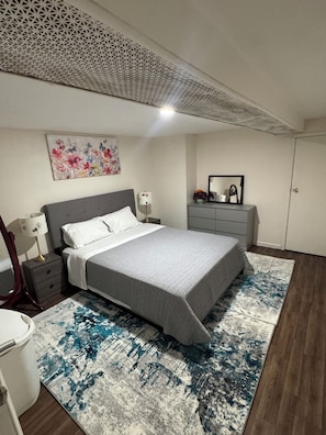 A bedroom with a bed, nightstands, a dresser, a mirror, and a ceiling with a geometric pattern. - Cozy 1-bedroom house in lovely Jamaica with AC (Jamaica)