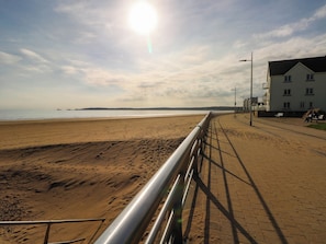A beach with a metal railing, a clear sky, and a building with multiple windows. - 21 Ferrara Square (Swansea)