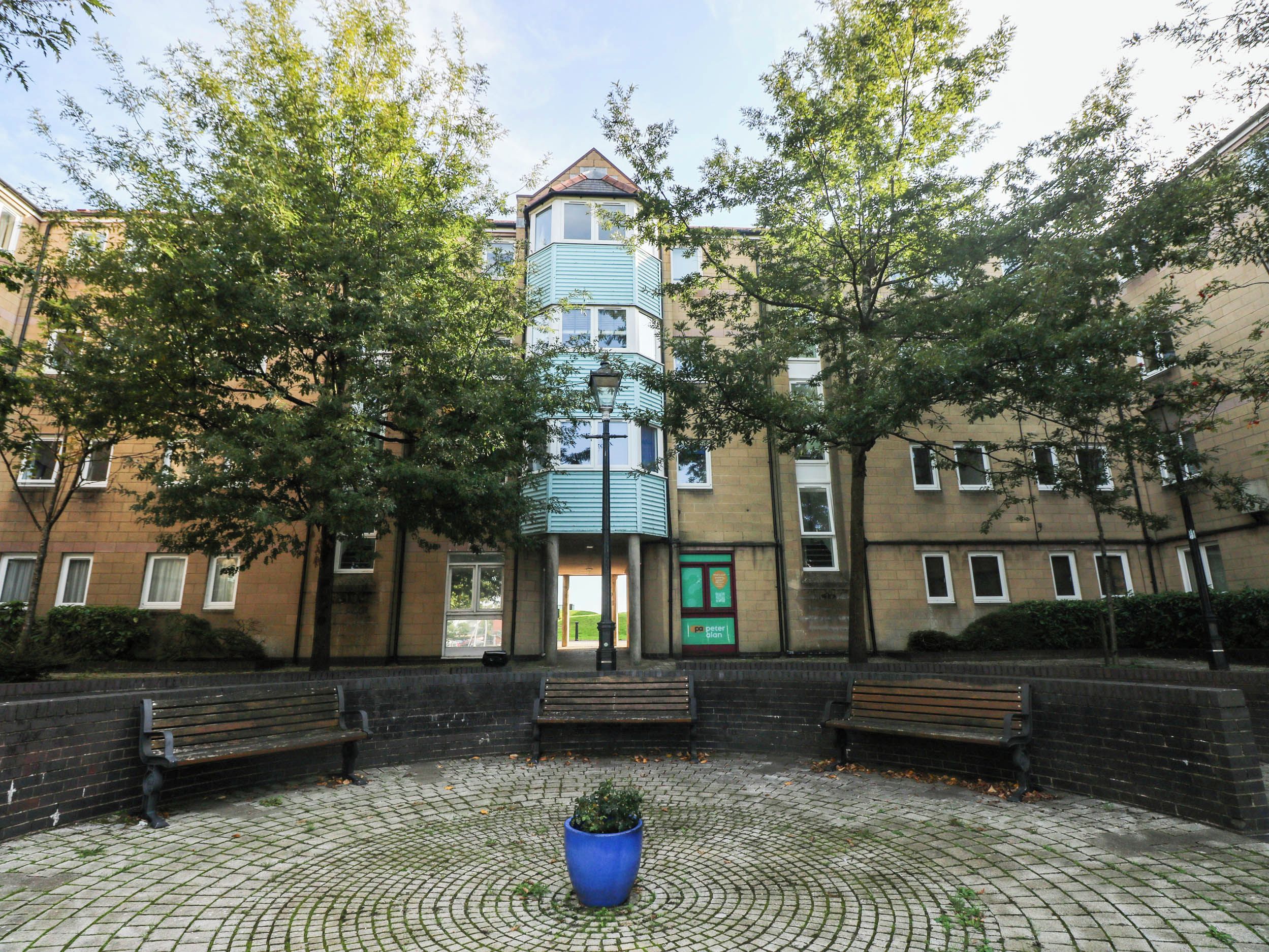 A courtyard with a central blue planter, surrounded by brick walls and benches.