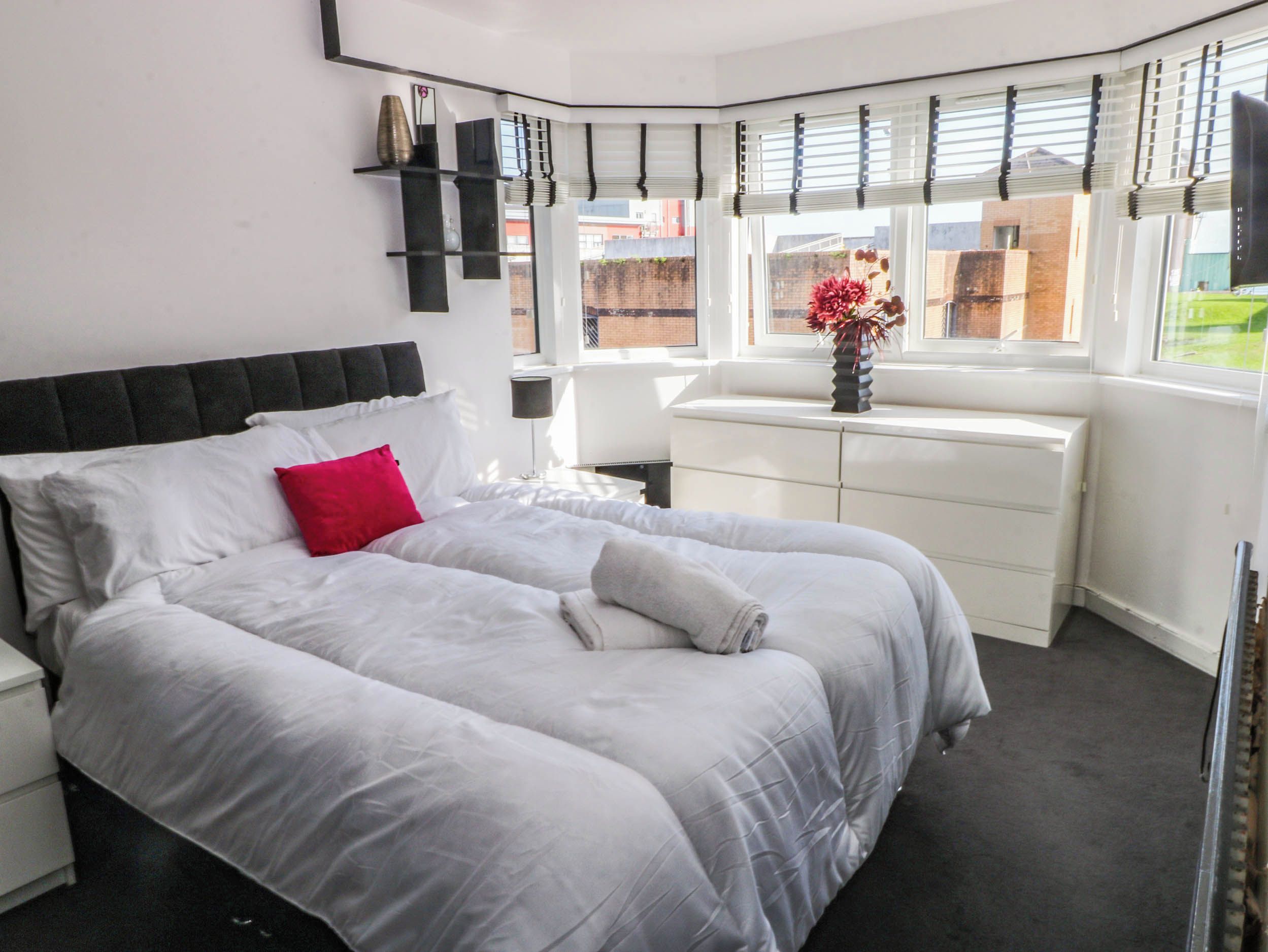 A bedroom with a bed, a nightstand, a dresser, and a window with blinds.