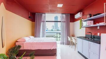 A modern hotel room with a bed, a small kitchenette, and a view of the city.