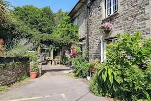 A stone building with a paved pathway leading to a wooden bench. - Bryher Cottage (Newquay)