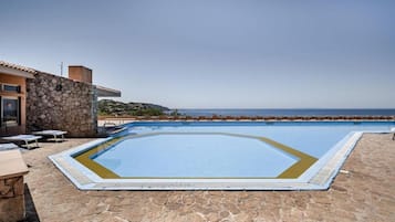 Una piscina con deck de piedra, un edificio con fachada de piedra y vistas al mar.