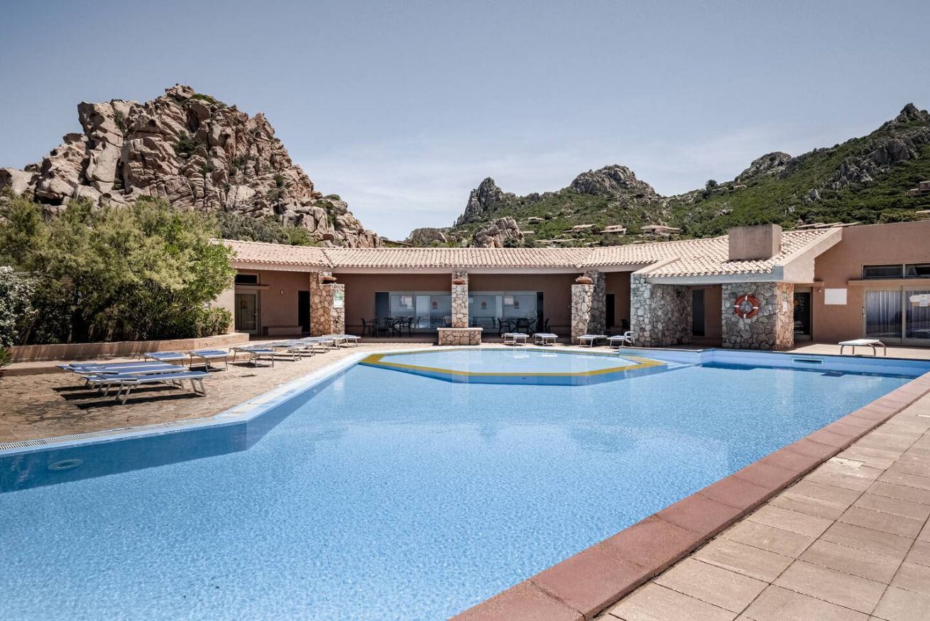 A swimming pool with lounge chairs, a stone building, and a mountainous backdrop.