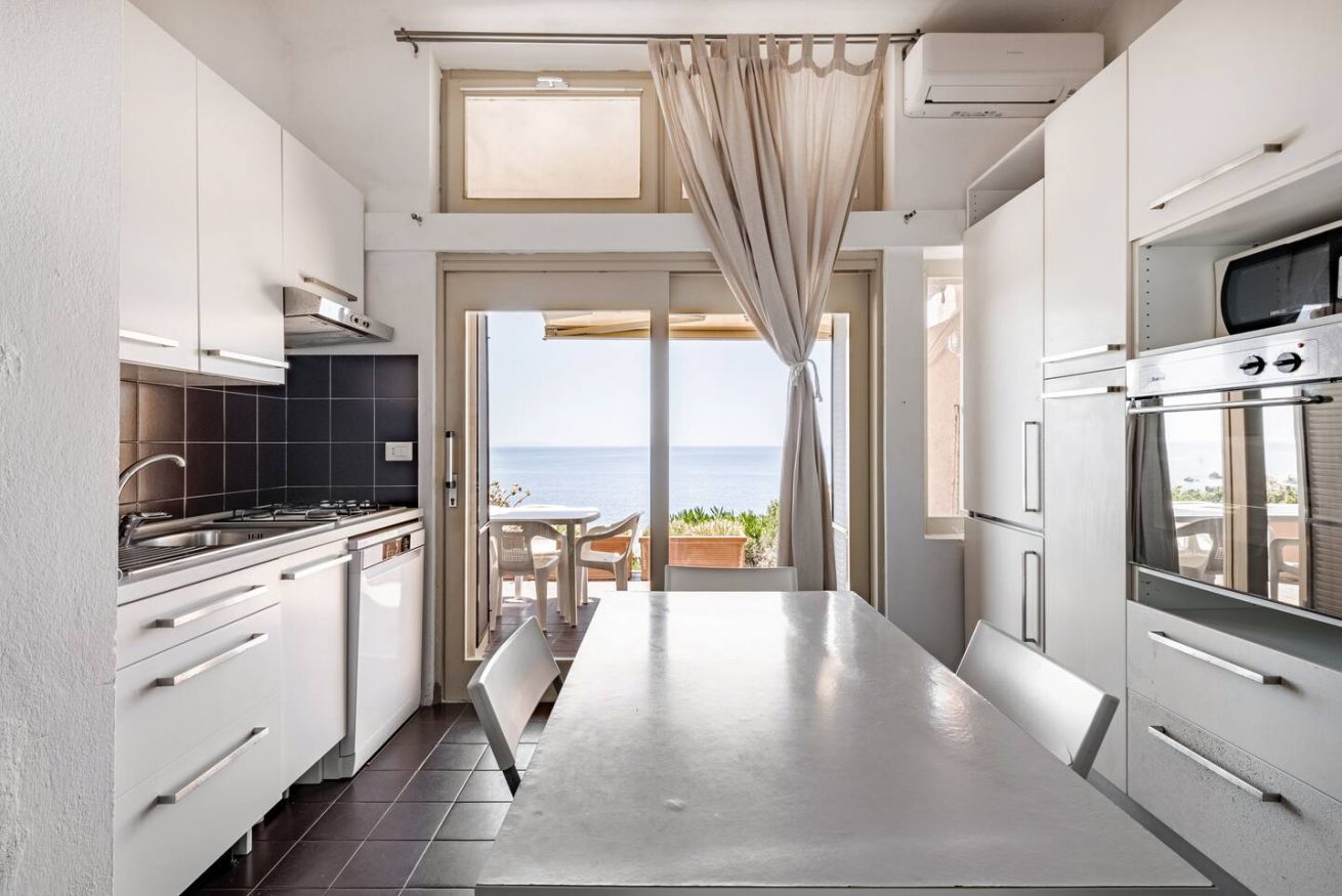 Eine moderne Küche mit Meerblick, ausgestattet mit einer großen Kochinsel, Backofen und weißen Schränken.