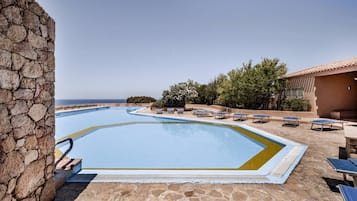Ein Swimmingpool mit einer Steinsäule an einer Seite, umgeben von Liegestühlen und einem Gebäude mit einem Ziegeldach.