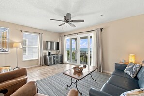 Ein geräumiges Wohnzimmer mit Deckenventilator, Flachbildfernseher, Essbereich mit Tisch und Stühlen sowie einer Couch mit dekorativen Kissen.
