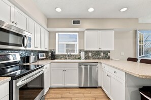 A modern kitchen with white cabinetry, stainless steel appliances, and a tiled backsplash. - Beachfront Retreat with Private Elevator (Indian Rocks Beach)