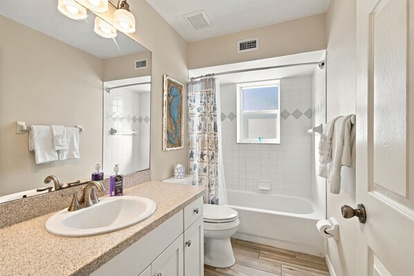 A bathroom with a double sink, a toilet, a bathtub, and a shower curtain. - Beachfront Retreat with Private Elevator (Indian Rocks Beach)