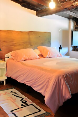 A bedroom with a wooden headboard, a bed with pink bedding, a bedside lamp, and a rug with a geometric pattern. - Holiday Home 'Casa Yañez Duplex' with Mountain View, Shared Garden and Wi-Fi (Chantada)
