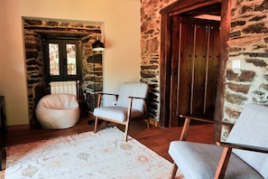 A room with a stone wall, a wooden door, a white bean bag chair, and two armchairs. - Holiday Home 'Casa Yañez Duplex' with Mountain View, Shared Garden and Wi-Fi (Chantada)