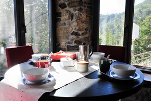 A dining table with various dishes and a coffee pot, set against a stone wall with a view of a forested area. - Casa de vacaciones 'Casa Yañez' con vistas a la montaña, terraza y Wi-Fi (Chantada)