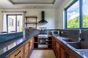 A modern kitchen with a gas stove, a microwave, and a built-in oven. There is a window providing a view of greenery outside. - 2bedroom apartment in Diani Beach with AC, Internet, private access to the beach (Diani Beach)