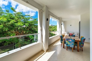 A balcony with a view of trees and sky, a dining table with chairs, and a window with curtains. - 2bedroom apartment in Diani Beach with AC, Internet, private access to the beach (Diani Beach)