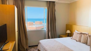 Habitación de hotel con cama, escritorio, televisor, ventana con cortinas y vista a edificios y agua.
