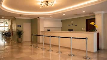 A hotel reception area with a check-in counter, a waiting line, and a clock on the wall.