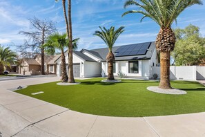 Ein Wohnhaus mit gepflegtem Rasen, Palmen und Solaranlage auf dem Dach.