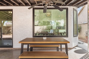 Eine Terrasse im Freien mit einem Holztisch und einer Bank, einem Deckenventilator und einem Fenster mit Jalousien.