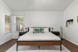 A bedroom with a bed, bedside tables, a window with blinds, and a wall-mounted plant. - 3 Bedroom/ Private Fenced Backyard /Desert Style (Gilbert)