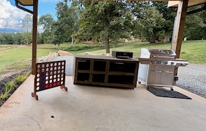 An outdoor patio with a grill, a wooden board game, and a concrete floor.