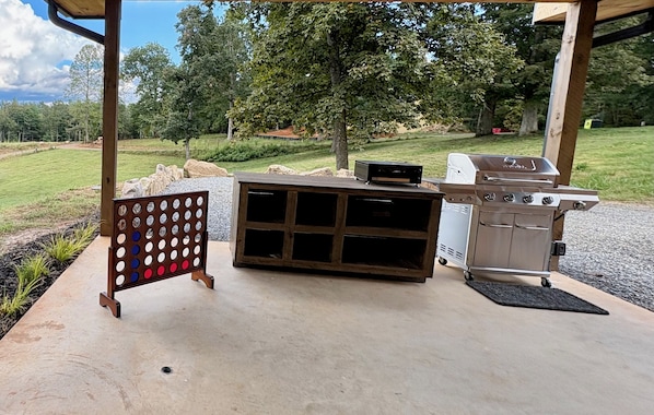 Un patio exterior con una parrilla, un juego de mesa de madera y suelo de hormigón.