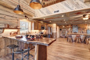 Una cocina rústica con armarios de madera, una isla grande con taburetes de bar y vistas al exterior a través de una ventana.