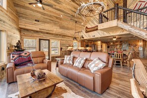 Interior espacioso de una cabaña de madera con un sofá de cuero, un comedor y una escalera que conduce a un nivel superior.