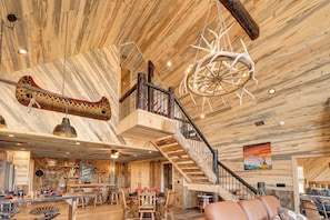 A spacious interior with a high ceiling, wooden beams, a large wooden wheel chandelier, and a staircase.