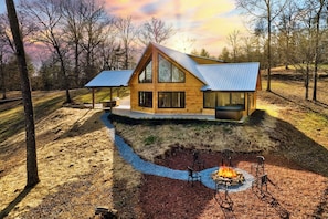 A wooden cabin with a large glass window, a fire pit, and outdoor seating.
