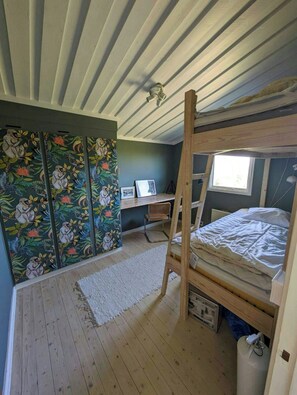 Ein Zimmer mit einem Etagenbett, einem Schreibtisch mit Computer, einem Heizkörper und einem Fenster.