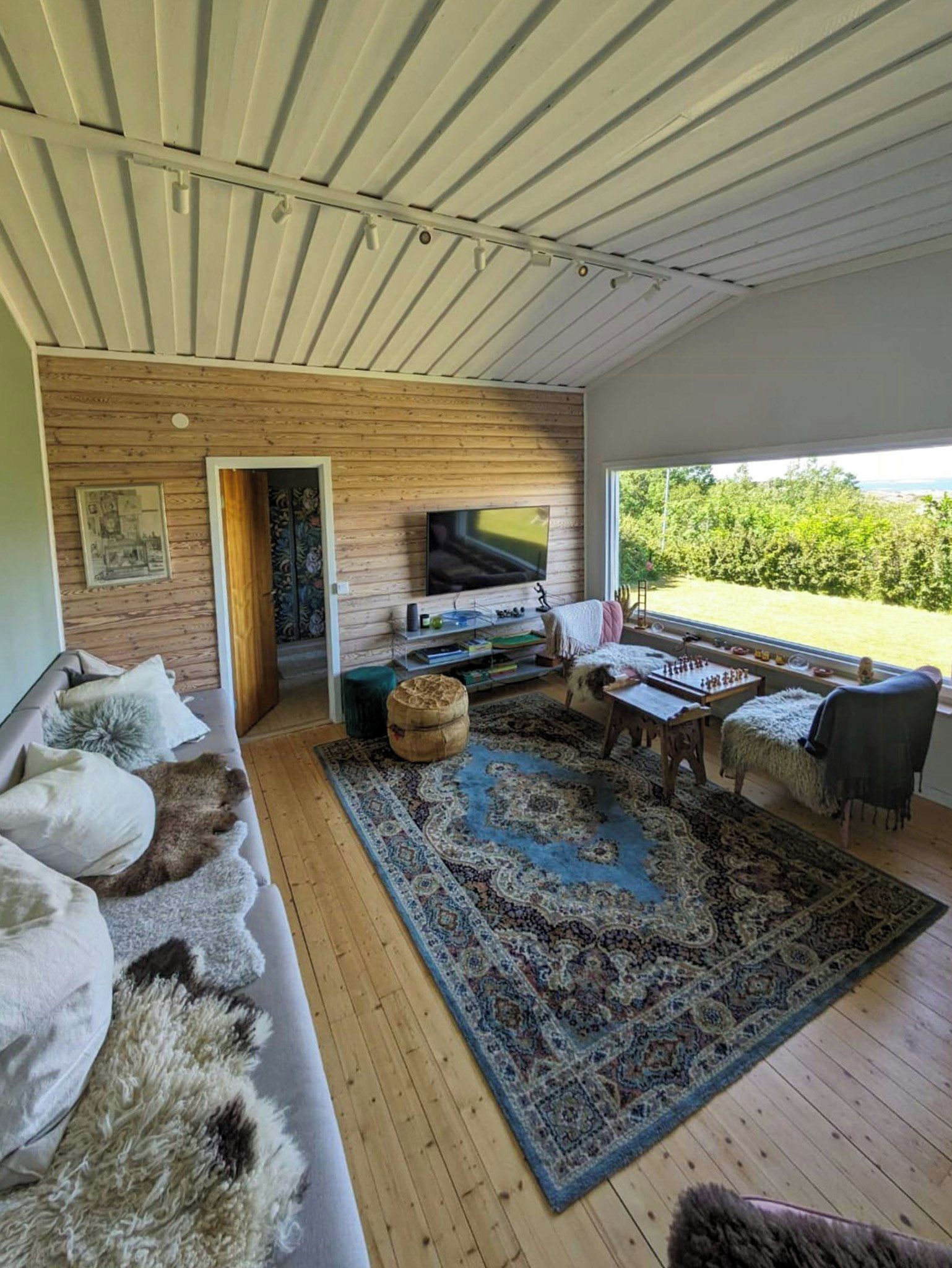 Una sala de estar moderna con piso de madera, un televisor grande, un sofá, una mesa de centro y vista a zonas verdes.