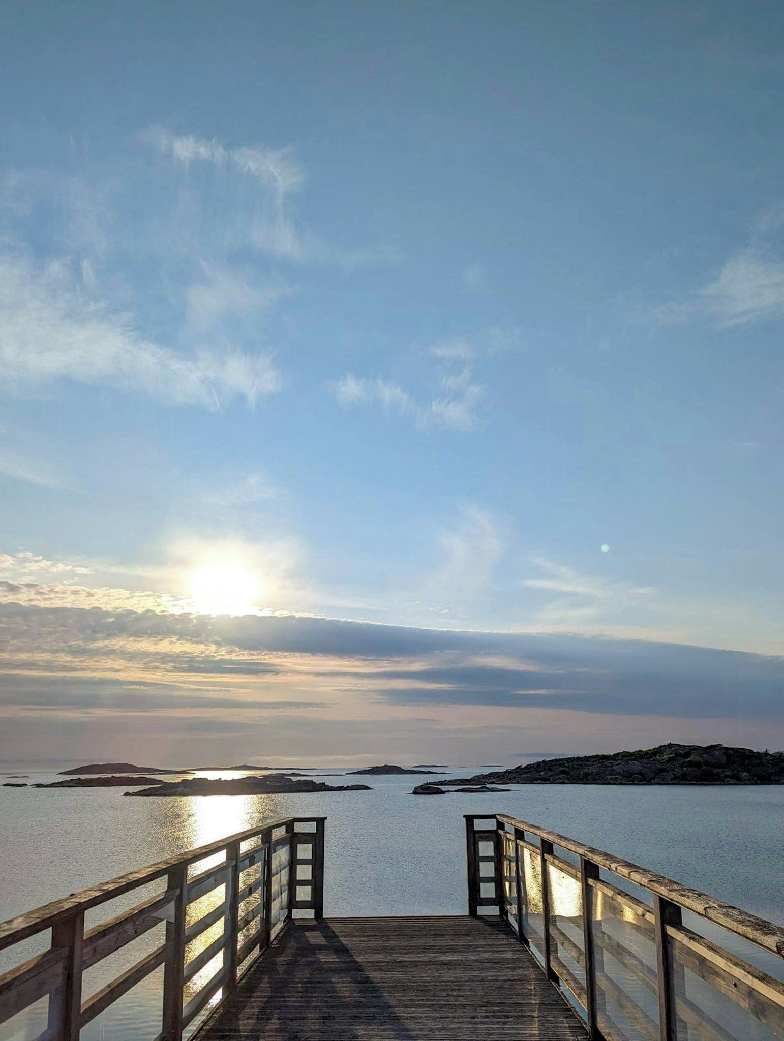 A wooden pier leading to calm waters with a clear sky and distant land.