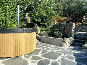 Ein hölzernes Whirlpoolbad, umgeben von Steinstufen und viel Grün.