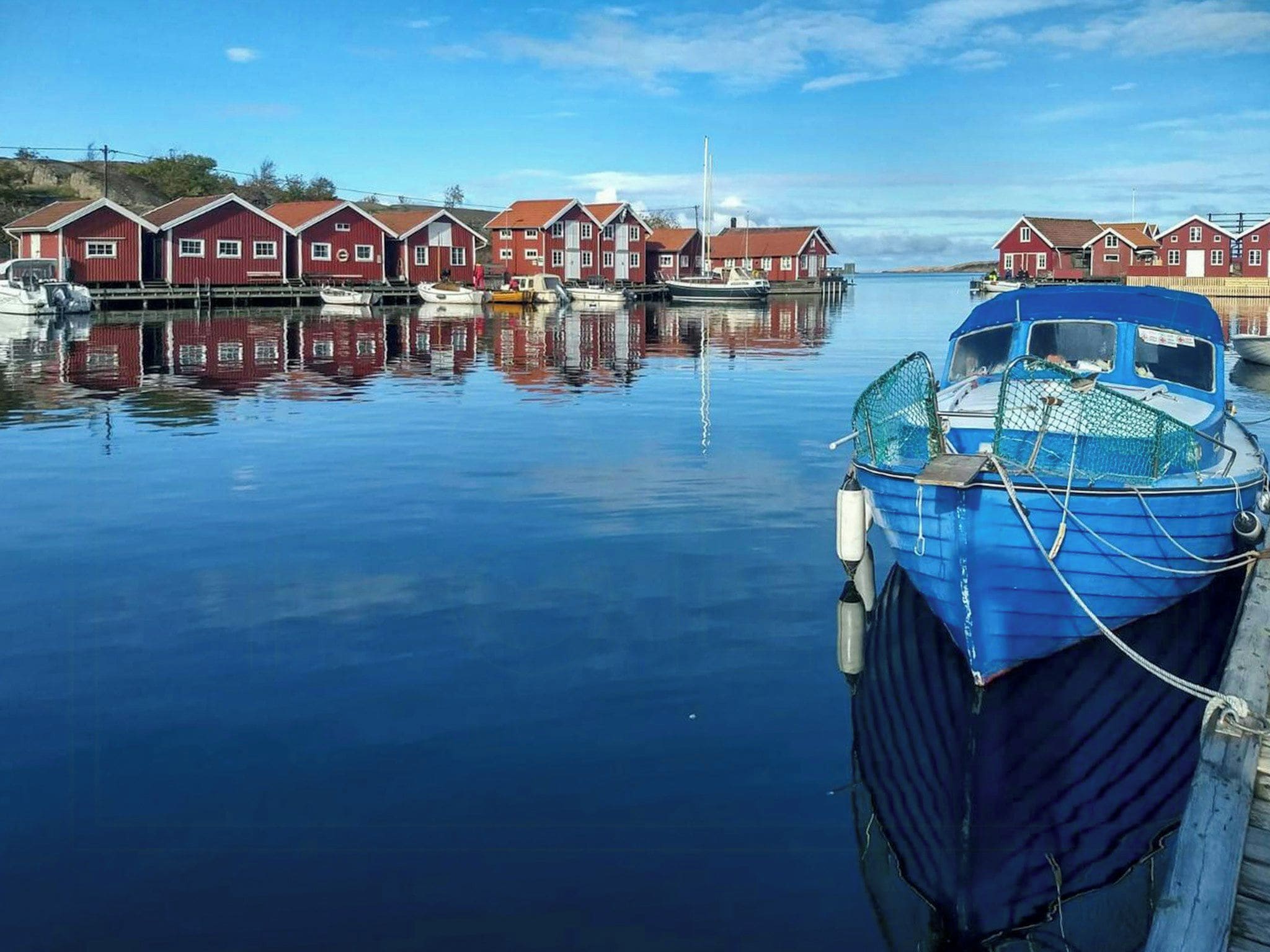 A calm harbor with red buildings and a blue boat docked.