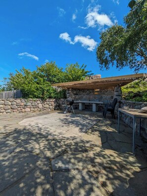 Eine Außenpatio mit einer Steinsäule, einer Holzpergola und einem Grill.