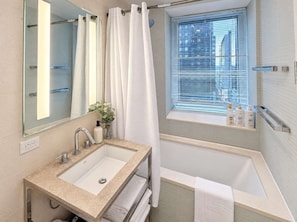 A modern bathroom with a large sink, a bathtub, a window with blinds, and a mirror.