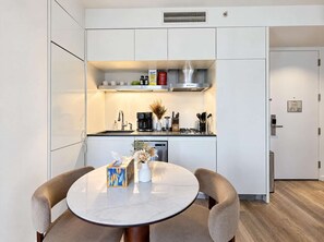 A modern kitchen with a built-in oven, coffee maker, and various appliances. There is a dining table with chairs and a vase with flowers.