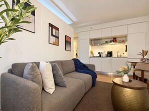 Ein modernes Wohnzimmer mit einer Couch, Kissen, einem Couchtisch und einer Küche im Hintergrund.