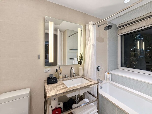 A modern bathroom with a large mirror, a sink, a shower, and a window with a city view.