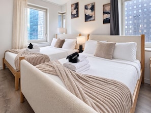 A hotel room with two beds, a window with a city view, and artwork on the wall.