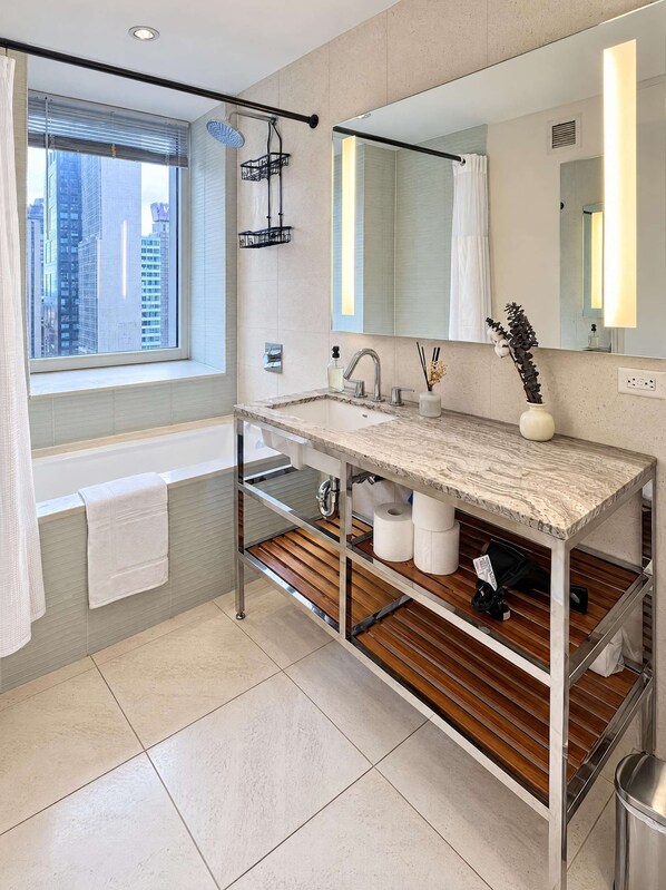 A modern bathroom with a large window, a bathtub, a vanity with a mirror, and a shelf with toiletries.