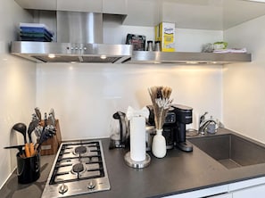 A modern kitchen with a stainless steel range hood, a gas stove, a coffee maker, and a kettle.