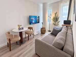 Un salon moderne avec un téléviseur à écran plat, une table ronde, deux chaises, un canapé et une lampe sur pied.