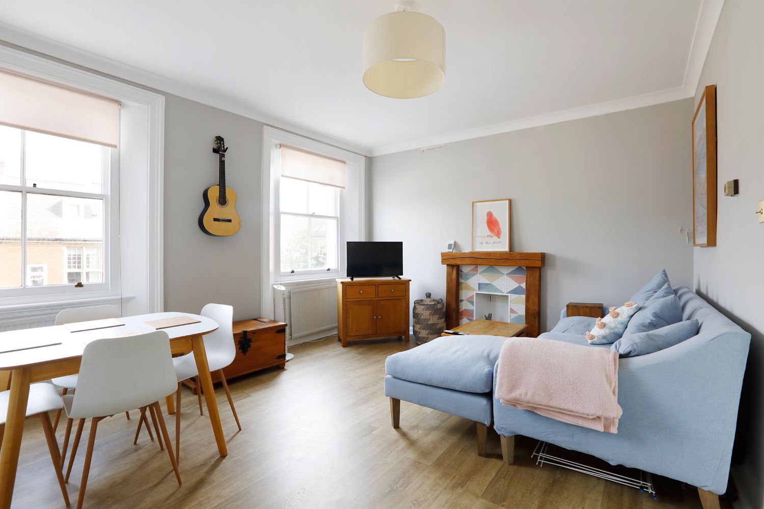 Een woonkamer met een blauwe bank, een eettafel met stoelen, een gitaar, een televisie en een open haard.